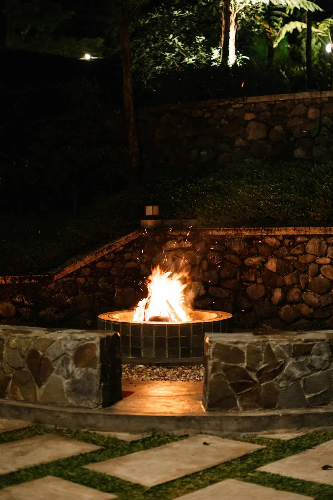 Gas fire pit glowing at night beside a stone wall